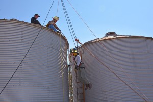 Jarett Depizzol of the Justice Rural Volunteer Fire Department (center, in harness) is hoisted through the air to the top of a grain bin on the farm of Kelly Harris in the Justice community near Spring Hope as part of a rope rescue training exercise. Depizzol is also a student in the College Transfer program at VGCC. Seated on top of the bin are, from left, instructor Joe Burris and Russell Bottoms of the Louisburg Fire Department. (VGCC photo)