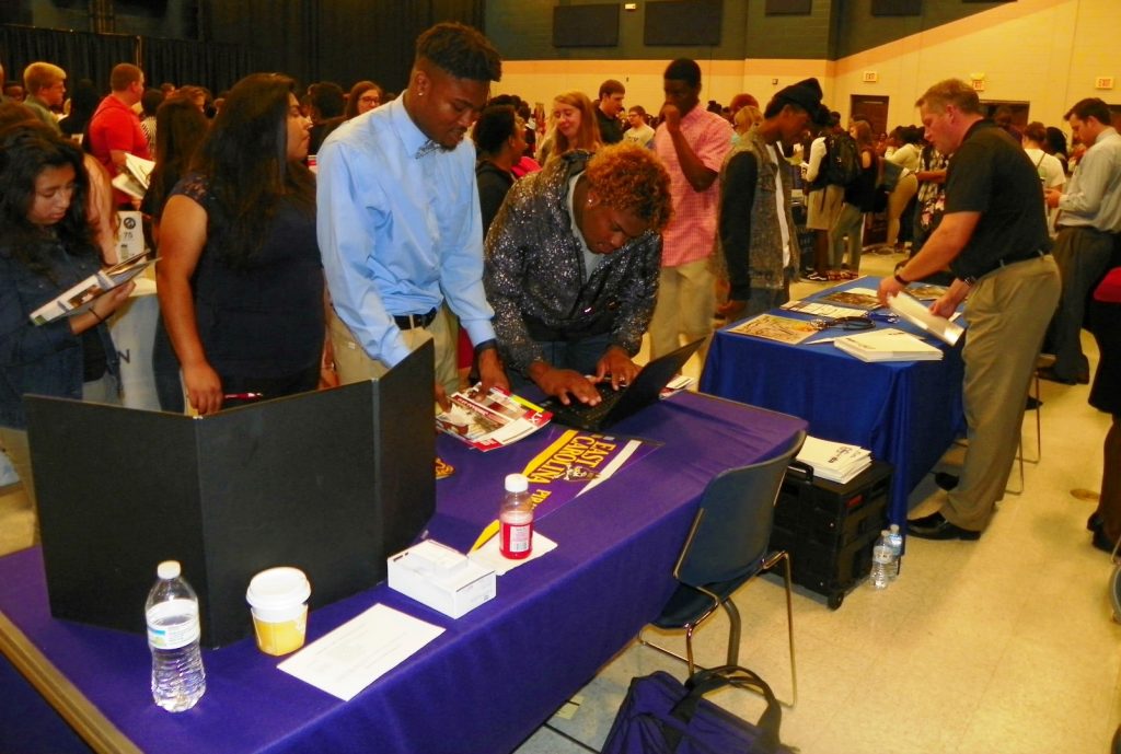 Students complete information at the table for East Carolina University in a crowded Civic Center at Vance-Granville Community College during the annual College Fair event.